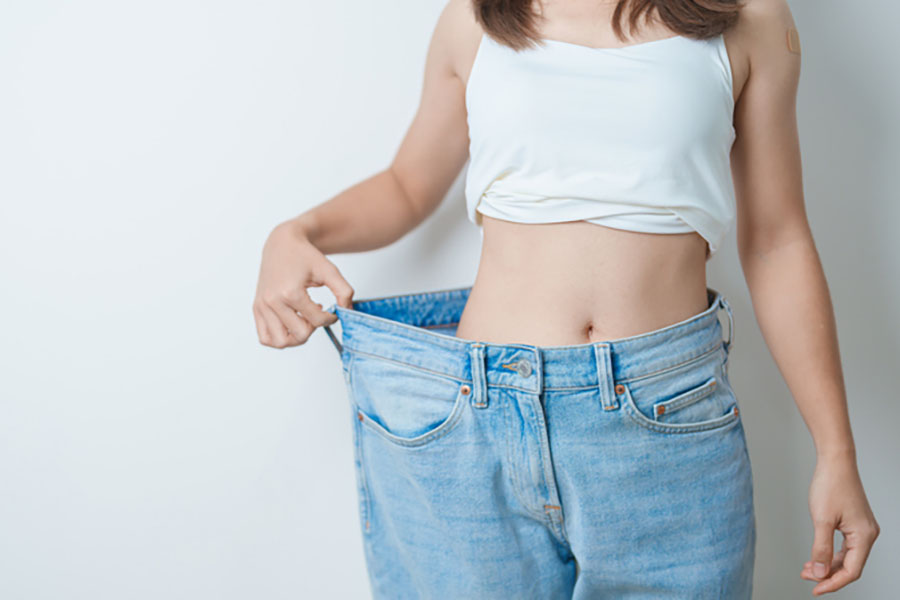 Woman showing rapid fat loss success by standing in oversized jeans that no longer fit her waist