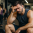 Mann sitzt auf einer Bank im Fitnessstudio, der nach dem Krafttraining und zu viel Junk-Volume müde aussieht