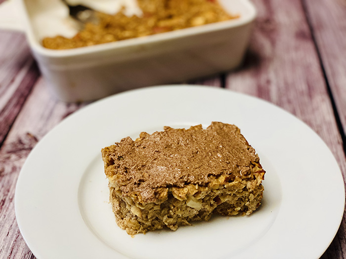 Gebackener Haferbrei mit Apfel-Zimt-Protein, von dem eine Scheibe aus der Form genommen und im Vordergrund auf einem Teller serviert wurde, wodurch die weiche, gebackene Textur sichtbar wird