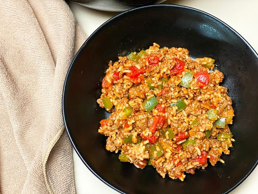 Schwarze Schüssel mit spanischem Eintopf mit Reis und Hackfleisch neben einem Küchentuch