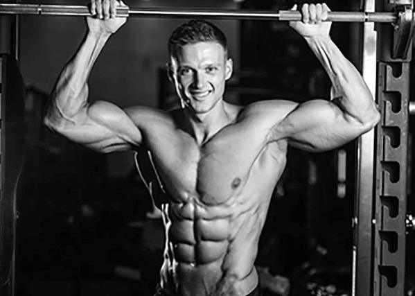 Ein Mann, der mit angespannten Armen und gut entwickelten Bauchmuskeln eine Hantelstange über Kopf hält