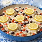 eine blaue Pfanne mit Griechischen Hähnchenoberschenkel mit Reis, Zitronenscheiben, Oliven und Feta