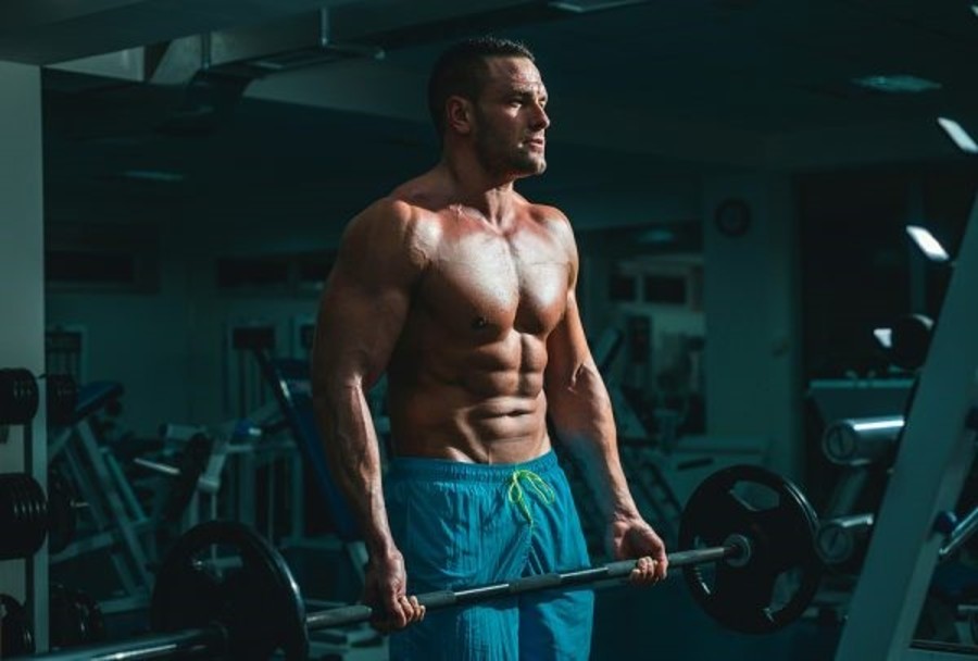 Ein Mann in blauen Shorts trainiert seinen Bizeps mit einer Langhantel