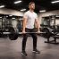 Athletischer Mann im Fitnessstudio führt eine Romanian Deadlift (Langhantel-RDL) in aufrechter Startposition mit schwerer Langhantel aus