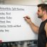 Muskulöser Mann im Fitnessstudio schreibt Trainingsplan für eine wöchentliche Split-Routine auf ein Whiteboard