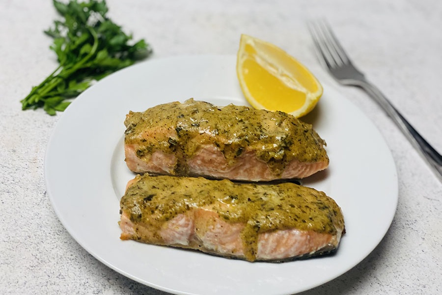 Zwei Stück Senf-Lachs auf einem Teller mit einer Zitronenscheibe