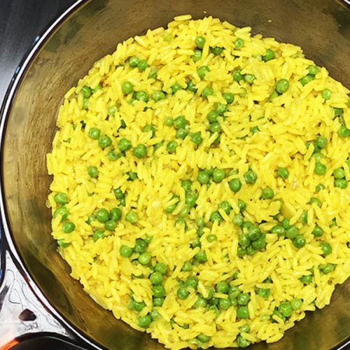 Eine Pfanne mit Kurkuma-Reis und Erbsen auf dem Herd