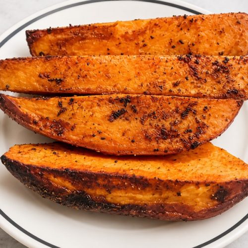 Würzige Süßkartoffel-Wedges aus dem Ofen mit gebräunten Rändern auf einem weißen Teller.